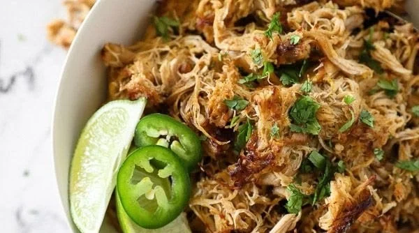 Plate of crispy chicken carnitas topped with cilantro and lime